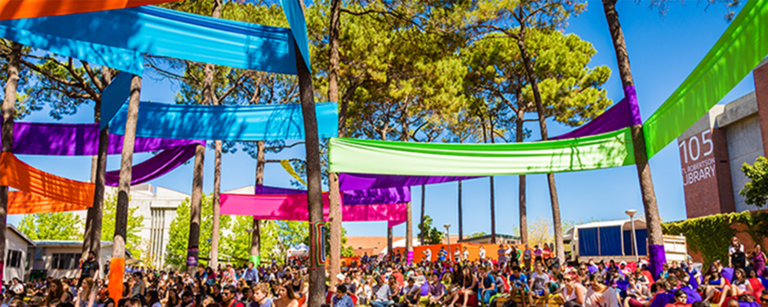 Bright coloured flags between trees and diverse people sitting underneath